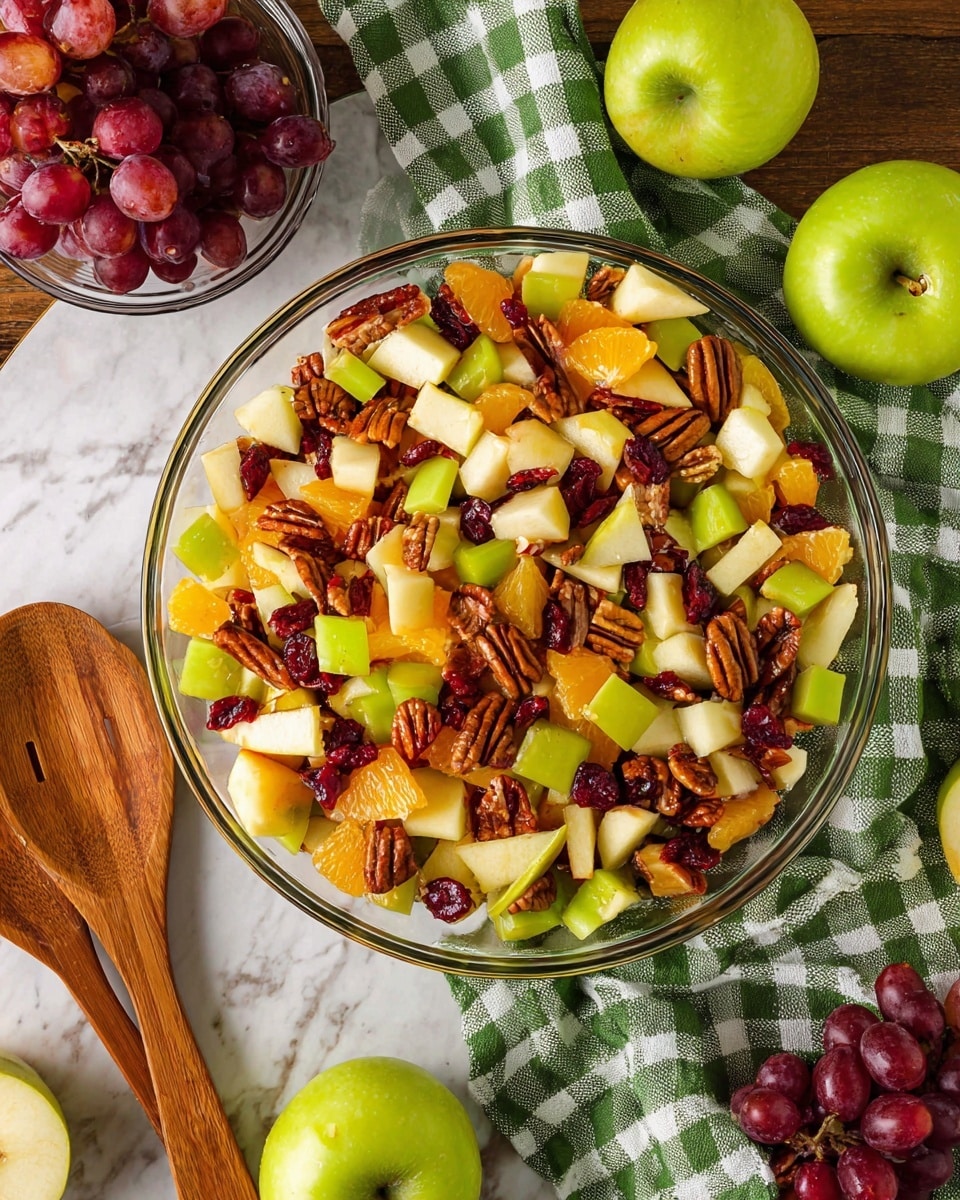 The image shows a clear glass bowl full of fresh fruit salad placed on a white marbled surface. The salad has many small cut pieces of green and red apples, orange slices, red grapes, pecan nuts, and dried cranberries, all mixed evenly. Around the bowl, there are whole green apples, both whole and cut in half, as well as a small clear bowl filled with red grapes. A green and white checkered cloth and wooden salad servers are near the bowl, adding a cozy touch. The photo taken with an iphone --ar 4:5 --v 7