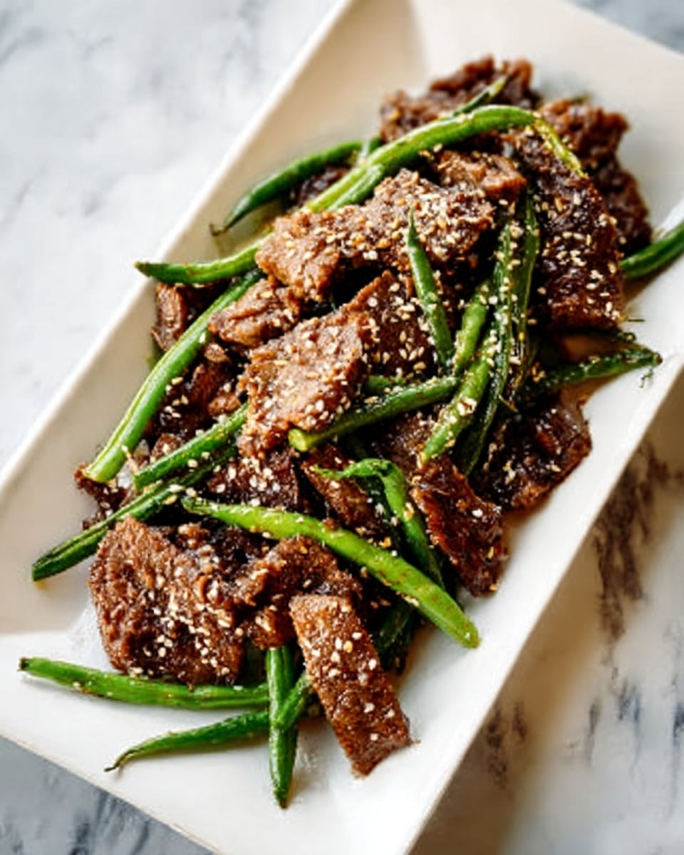 A white rectangular plate holds several pieces of cooked, browned meat covered in a sprinkling of sesame seeds. The meat appears tender with a slightly glossy and textured surface. Long, slender green beans are placed on top and among the meat pieces, adding a fresh green color contrast. The plate is set on a white marbled surface with a soft natural light highlighting the rich colors and textures. Photo taken with an iphone --ar 4:5 --v 7
