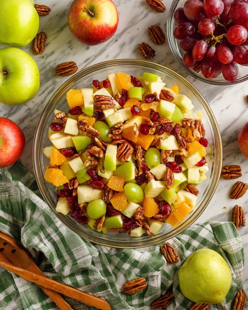 A clear glass bowl filled with a colorful fruit salad sits on a white marbled surface. The salad has many layers of diced green and red apples with white flesh, small round red grapes, bright orange chunks of orange, brown pecan nuts, and small pieces of dark red dried cranberries scattered on top. Around the bowl, there are whole green apples, some pecans, and a clear glass bowl with more red grapes. A green and white checkered cloth is draped at the bottom left, and wooden salad tongs rest on the surface near the bottom right. photo taken with an iphone --ar 4:5 --v 7