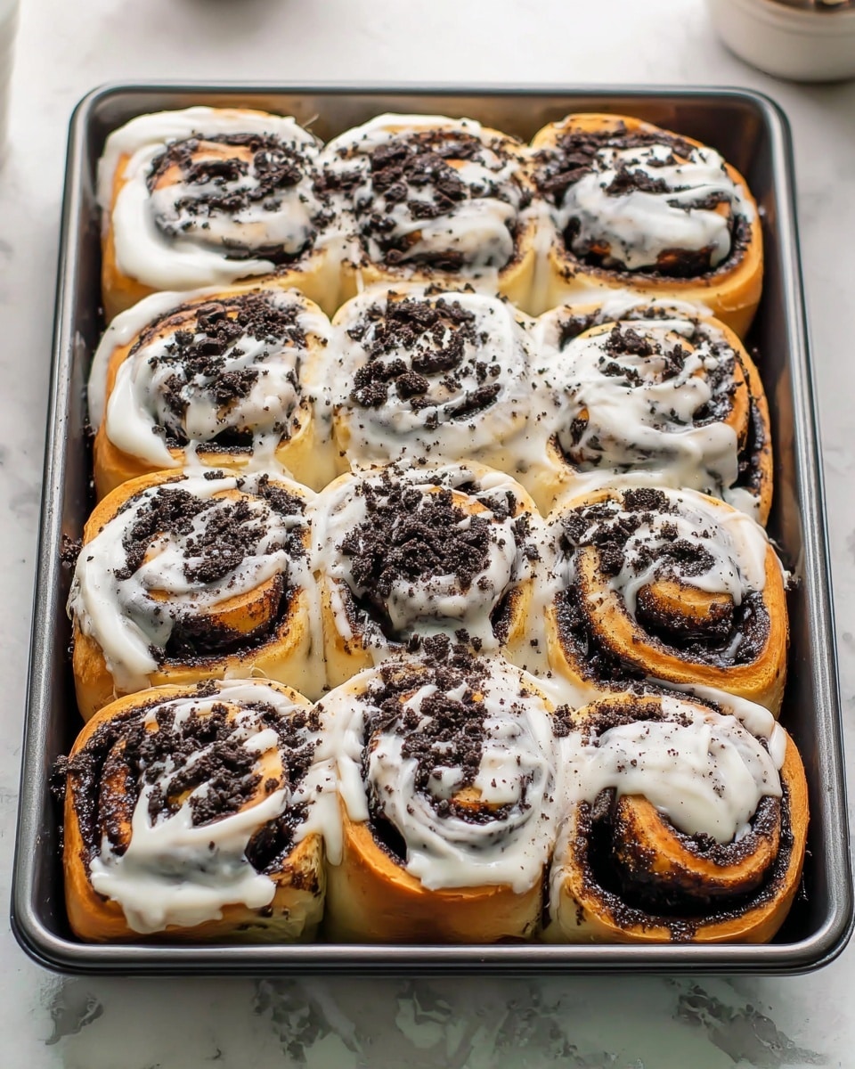 The image shows a baking tray filled with nine cinnamon rolls arranged in three rows of three. Each roll has multiple layers of light golden-brown dough with a dark, almost black filling swirled inside. The rolls are generously topped with thick white icing that is drizzled unevenly across the surface, creating a smooth and creamy texture. Crushed dark cookie crumbs are sprinkled over the icing, adding a crunchy contrast. The tray is placed on a white marbled texture surface, and the whole scene looks fresh and inviting. Photo taken with an iphone --ar 4:5 --v 7