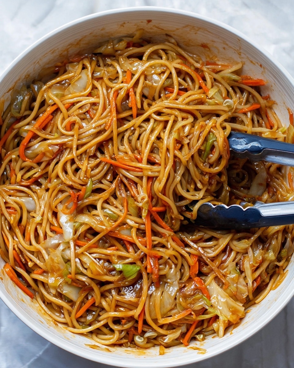 A large white bowl filled with stir-fried noodles mixed with thin strips of orange carrots and light brown cabbage pieces, all coated in a glossy brown sauce that gives the dish a shiny look; the noodles are long and tangled, with some strands lifted slightly by a pair of black and gray tongs resting inside the bowl. The background shows a white marbled surface. photo taken with an iphone --ar 4:5 --v 7