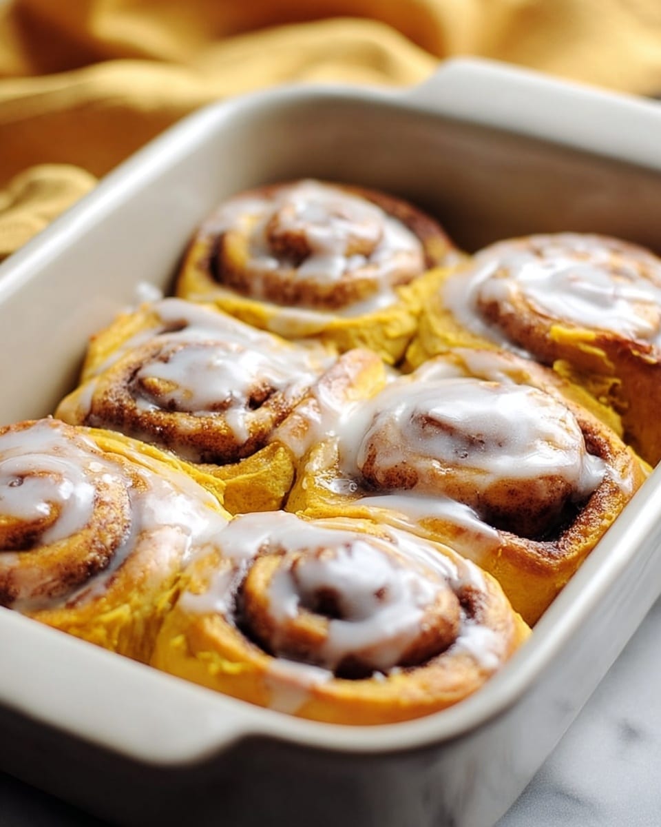 The image shows six pumpkin cinnamon rolls in a white rectangular baking dish. Each roll has a bright orange dough base, filled with dark brown cinnamon sugar spirals. They are topped with a creamy white glaze that partly covers the top surfaces and drips slightly on the sides. The rolls are tightly packed in two rows of three, showing soft and fluffy textures with swirled layers of filling inside each roll. The baking dish sits on a white marbled surface. photo taken with an iphone --ar 4:5 --v 7