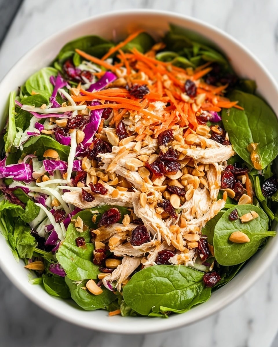 A fresh salad in a white bowl placed on a white marbled surface, showing three main layers: the bottom layer is dark green spinach leaves with leafy texture; the middle layer has bright orange thin carrot sticks and light purple shredded cabbage scattered evenly; the top layer includes white shredded chicken strips, light brown peanuts, and deep red dried cranberries sprinkled all over, adding color and texture contrast. photo taken with an iphone --ar 4:5 --v 7