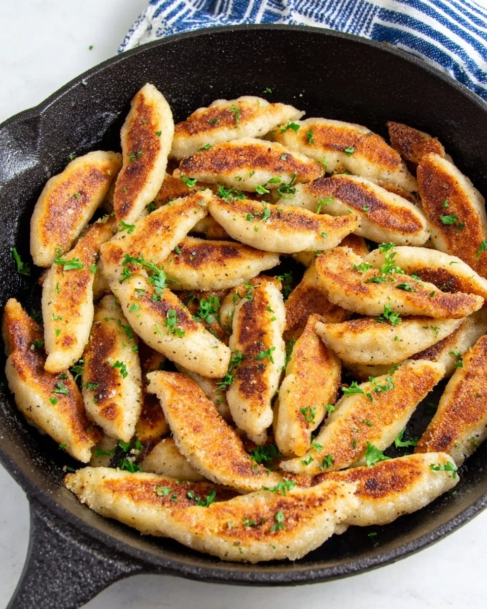 The image shows a black cast iron pan filled with browned, finger-shaped fried dumplings or bread pieces, each with a crispy golden-brown to light tan crust. The pieces are scattered in a slightly overlapping way, sprinkled with small bits of fresh green herbs. The pan sits on a white marbled surface with a blue and white striped cloth partly visible in the top part of the image. The texture of the dumplings looks soft inside with a crunchy outside. photo taken with an iphone --ar 4:5 --v 7
