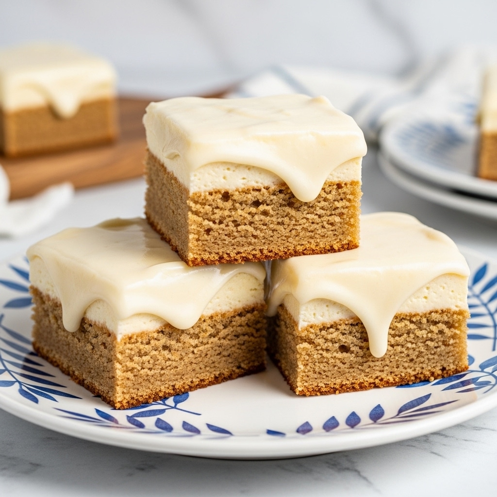 Three square bars of cake are stacked on a white plate with a blue leafy pattern. Each bar has two layers: a golden brown bottom cake layer with a soft, crumbly texture and a thick, glossy, smooth light cream-colored frosting layer on top. The cake bars are placed in a slightly uneven stack, showing the thick frosting dripping gently over the edges. The background has a white marbled texture with blurred elements of wood and another plate. photo taken with an iphone --ar 4:5 --v 7