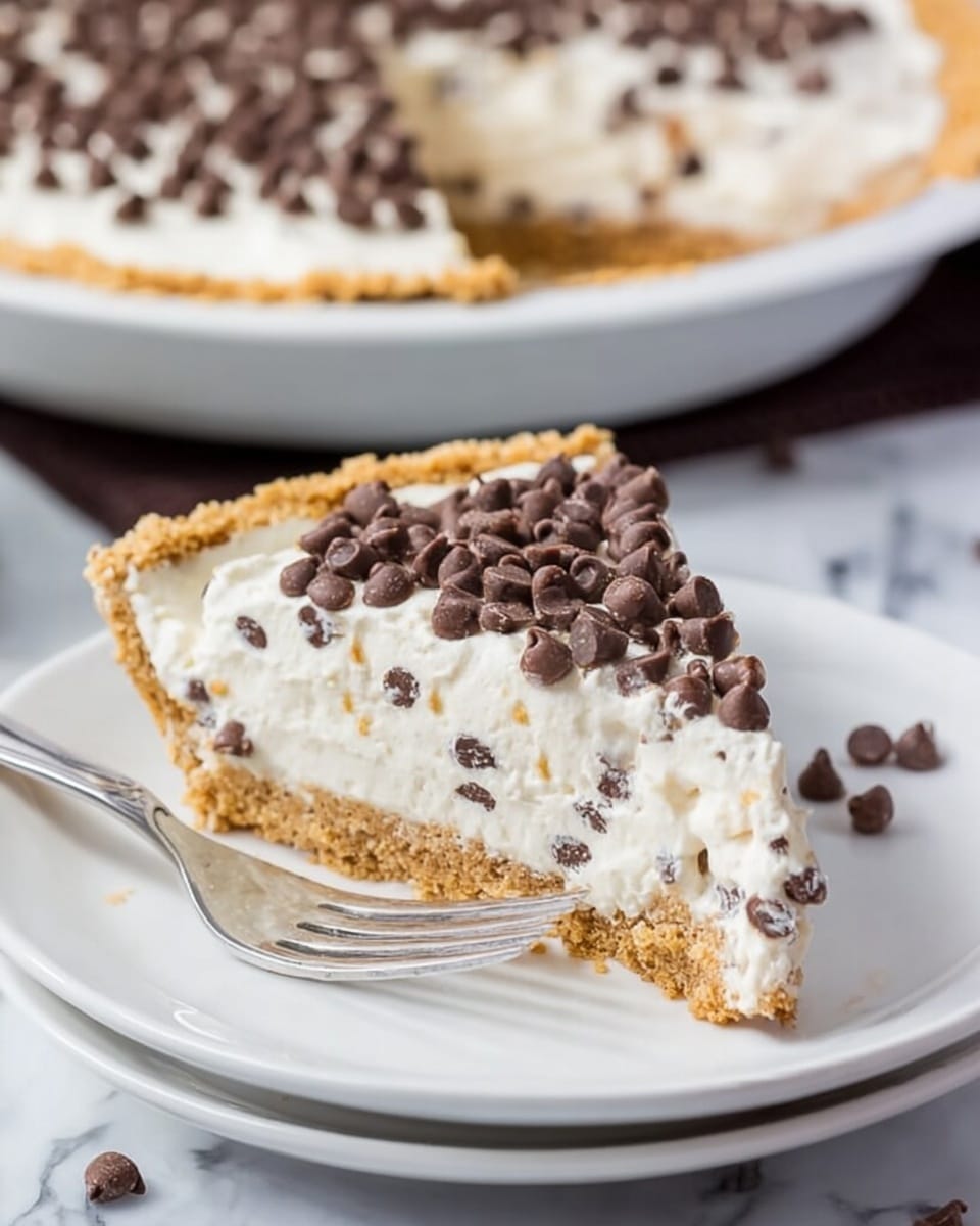 The image shows a slice of a creamy pie on a white plate with a silver fork beside it. The pie has three clear layers: a light brown crumbly crust at the bottom, a thick middle layer of white creamy filling mixed with small chocolate chips, and a top layer of white cream decorated with many small chocolate chips spread evenly. In the background, the rest of the pie sits on a white plate, with a woman’s hand partly touching it. The scene is set on a white marbled surface. photo taken with an iphone --ar 4:5 --v 7