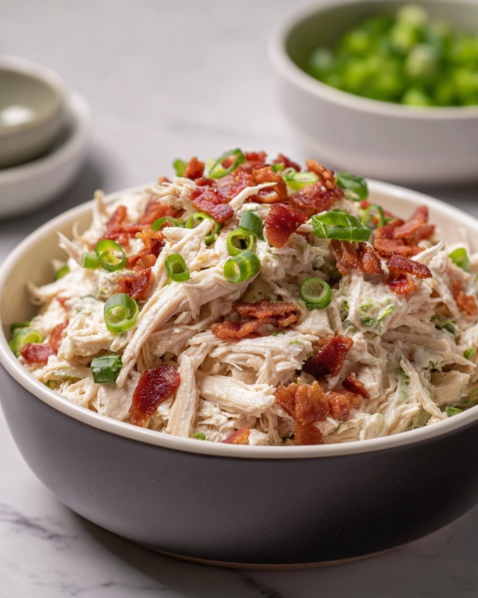 A close-up shot of a bowl filled with shredded chicken mixed with bacon bits and chopped green onions, showing the textures of tender white chicken strands layered throughout the mixture. Crispy brownish-red bacon pieces are scattered evenly across the top and inside, with small bright green spring onion slices adding color contrast. The bowl is white on the inside and dark on the outside, sitting on a white marbled surface. In the blurred background, there are two additional white bowls with some ingredients visible inside, enhancing the focus on the main dish. Photo taken with an iphone --ar 4:5 --v 7