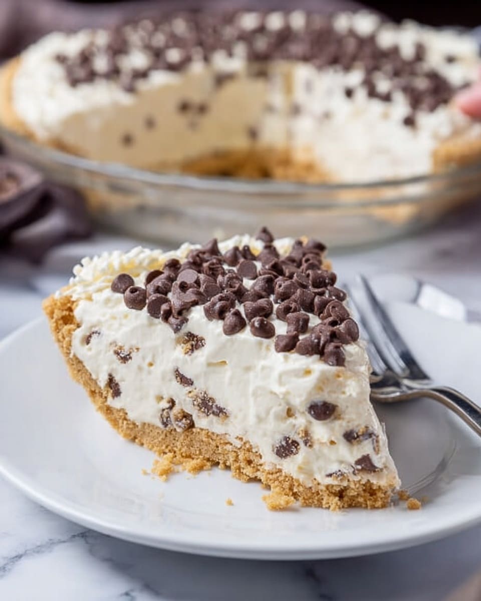 A slice of cream pie with a rough golden crust at the bottom, followed by a thick layer of white creamy filling mixed with small dark chocolate chips. The top layer is a smooth white cream spread evenly, covered densely with mini dark chocolate chips. The slice is placed on a white plate with a silver fork beside it, and more of the pie with a similar chocolate chip topping can be seen blurred in the background on a white plate. The surface under the plates is a white marbled texture. photo taken with an iphone --ar 4:5 --v 7