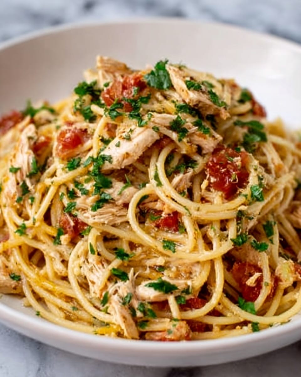 A white bowl filled with spaghetti pasta layered with small pieces of cooked chicken and sun-dried tomatoes, topped with finely chopped green herbs scattered across the dish. The pasta has a light shine showing it is well coated with olive oil or sauce, and the chicken pieces are white to light brown, mixed evenly throughout. The tomatoes add a rich red color, and the herbs give a fresh green contrast. The bowl sits on a white marbled textured surface. photo taken with an iphone --ar 4:5 --v 7