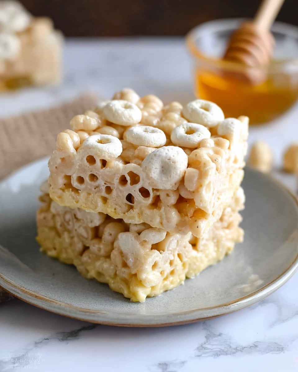 A square-shaped crispy treat sits on a white plate, made of light beige puffed rice cereal bound together with a creamy, slightly shiny white layer. On top, there is a scattering of pale yellow honeycomb-shaped candies and whole round nuts in cream tones, adding texture and visual interest. The edges of the treat are thick and irregular, showing the layers of cereal and binding clearly. In the background, a wooden honey dipper and a small clear bowl filled with amber honey sit on a white marbled surface, with blurred scattered nuts adding warmth and depth to the scene. Photo taken with an iphone --ar 4:5 --v 7
