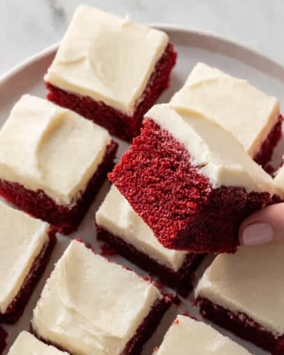 The image shows a white plate full of square red velvet cake pieces with smooth, thick white cream cheese frosting on top. One piece is slightly raised and held by a woman's hand, showing the deep red, soft-looking cake inside with a moist texture. The frosting is creamy and evenly spread, covering the entire top layer of each piece. The background features a clean white marbled surface. photo taken with an iphone --ar 4:5 --v 7
