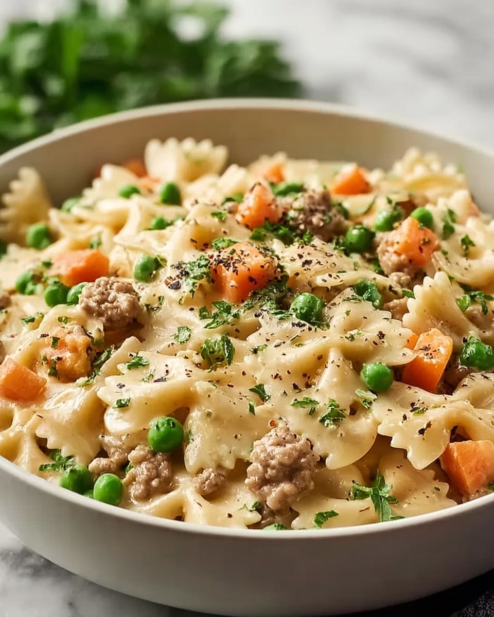 A white bowl filled with creamy pasta made of farfalle noodles, mixed with orange carrot cubes, bright green peas, and small brown pieces of ground meat, all covered in a smooth light beige sauce. The dish is sprinkled with finely chopped green parsley and a little black pepper, adding texture and color contrast. The bowl sits on a white marbled surface with a bunch of fresh parsley in the background and a silver spoon nearby. photo taken with an iphone --ar 4:5 --v 7